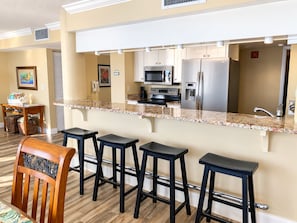 A modern kitchen with a bar area, stainless steel appliances, and a wooden chair. - Updated Direct Oceanfront - 3 bedroom #1007; Beach Access and Heated Pool (Daytona Beach Shores)