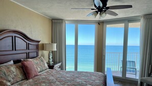 A hotel room with a large bed, a ceiling fan, a nightstand with a lamp, and a view of the ocean through large windows. - Updated Direct Oceanfront - 3 bedroom #1007; Beach Access and Heated Pool (Daytona Beach Shores)