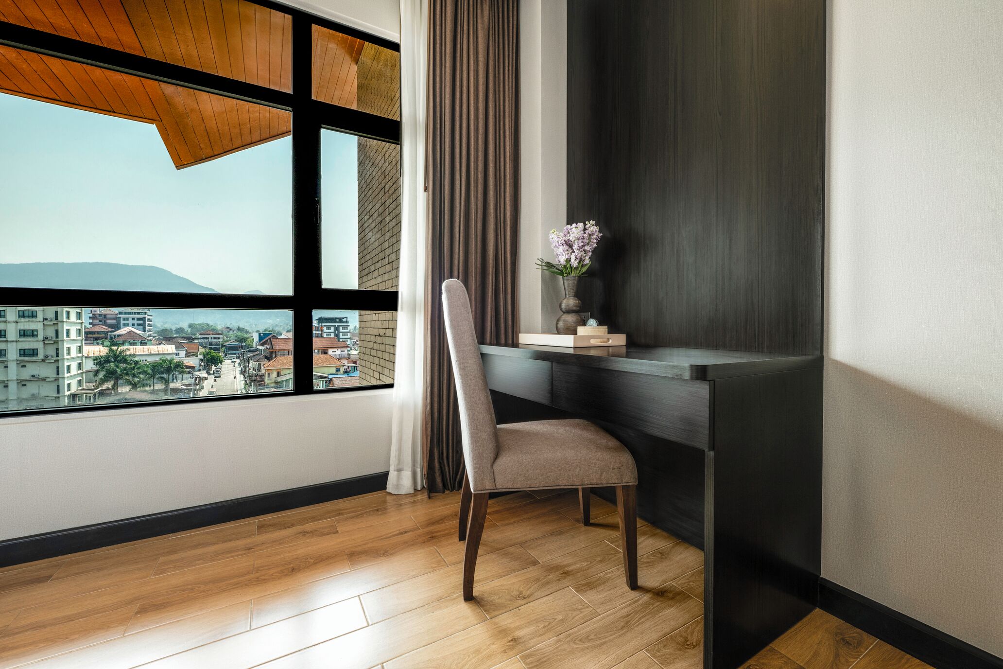 Een moderne kamer met een groot raam, een bureau, een stoel en een vaas met bloemen.
