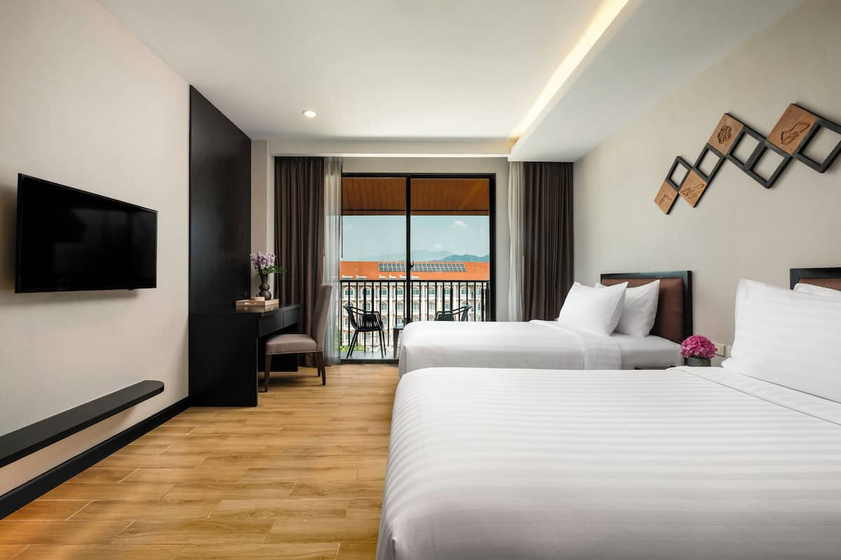 Ein Hotelzimmer mit zwei Betten, einem Fernseher, einem Schreibtisch, einem Sessel und einem Balkon mit Blick.