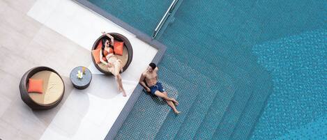 Zona de piscina con sillones reclinables y un hombre sentado junto a la piscina.