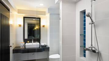 Un baño moderno con cabina de ducha de vidrio, inodoro blanco y lavamanos con espejo.
