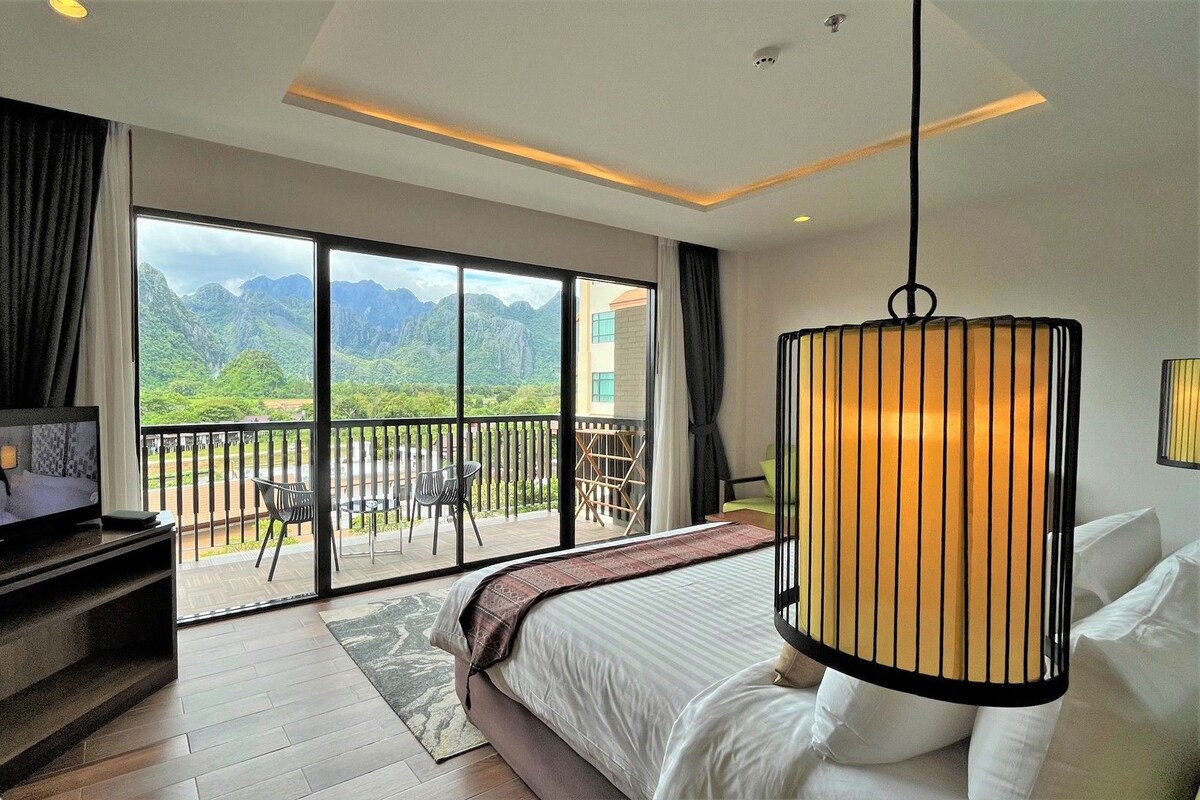 A hotel room with a balcony, a TV, a bed, and a hanging light fixture.