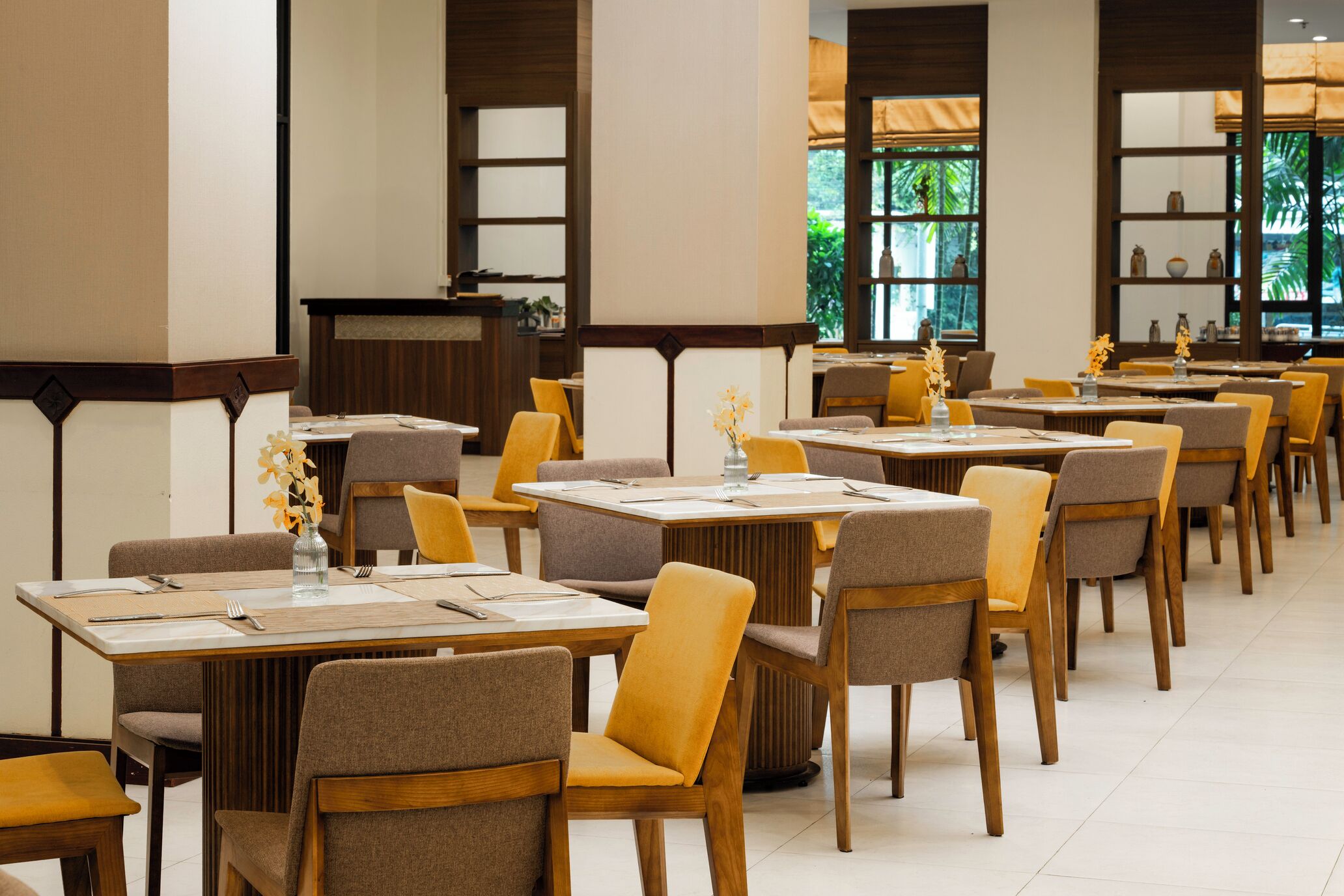 Un restaurant doté de nombreuses tables et chaises, d’un comptoir et de grandes fenêtres donnant sur un espace verdoyant.