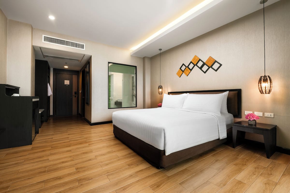 A hotel room with a bed, bedside table, lamp, and a desk with a chair.