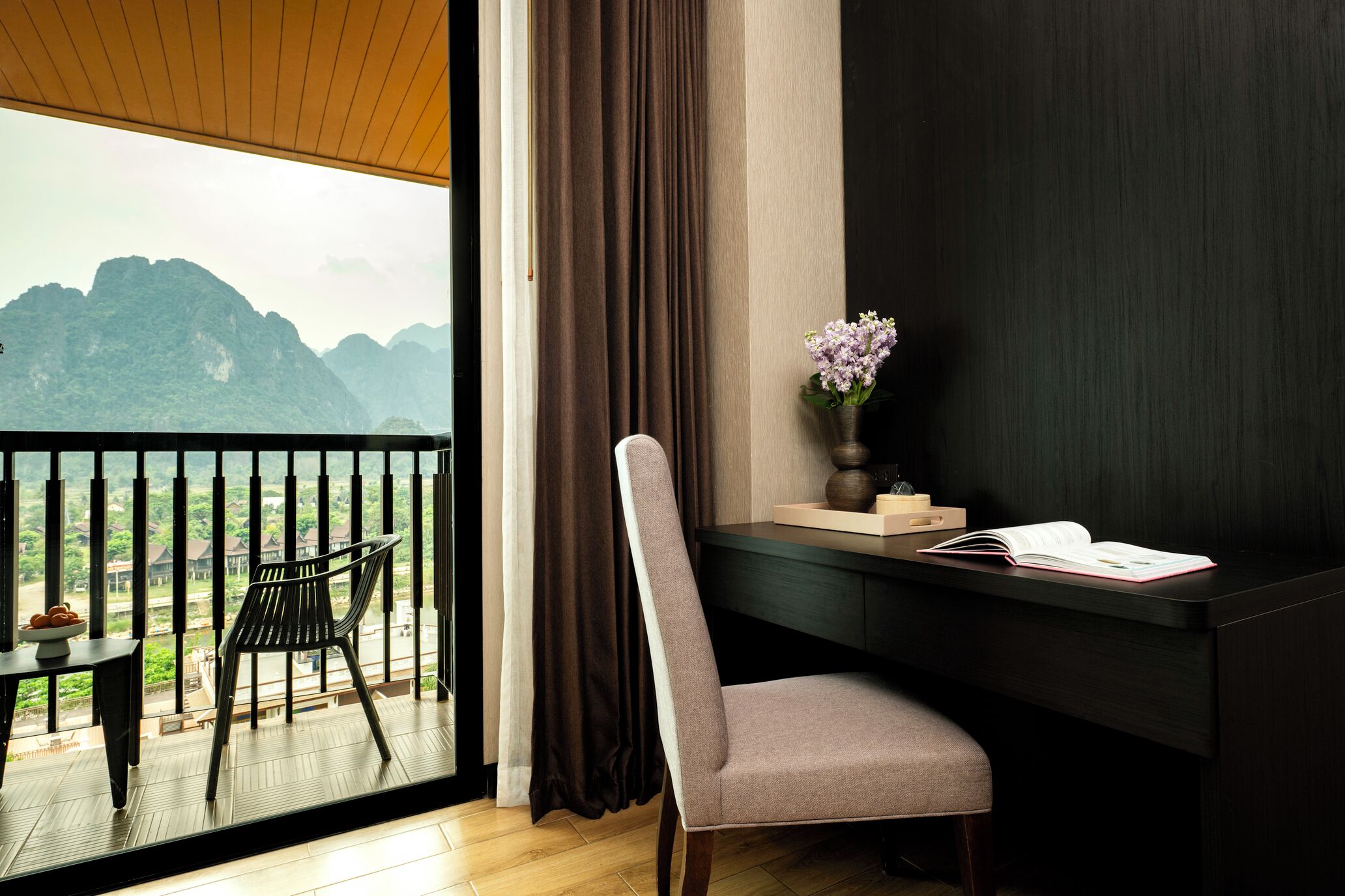 A room with a desk, chair, and a view of mountains through a balcony.