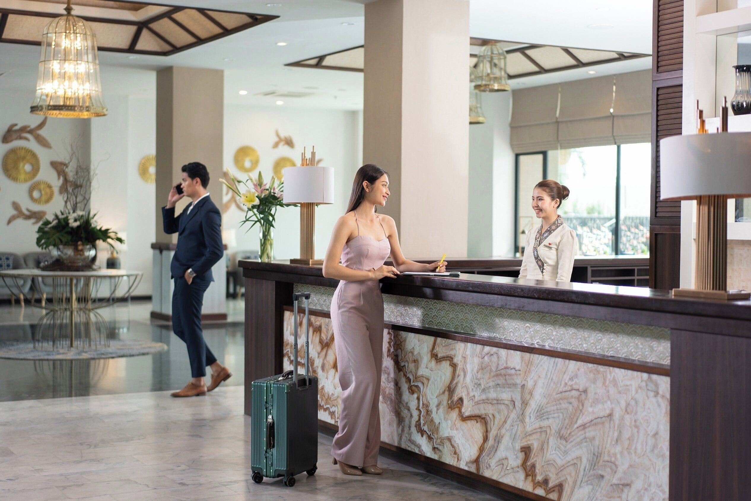 A hotel reception area with a marble counter, a large chandelier, and a modern interior design.