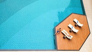 Una piscina en la azotea con terraza de madera y sillones de descanso.