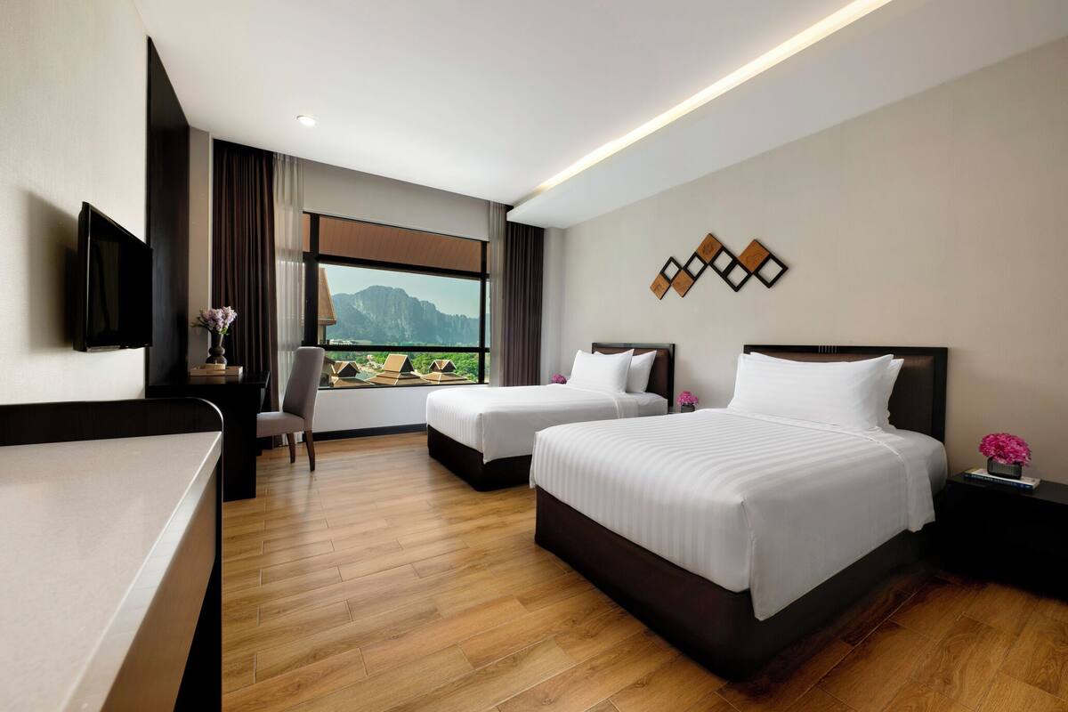 Ein Hotelzimmer mit zwei Betten, einem Schreibtisch, einem Sessel, einem Fernseher und Blick auf die Berge.