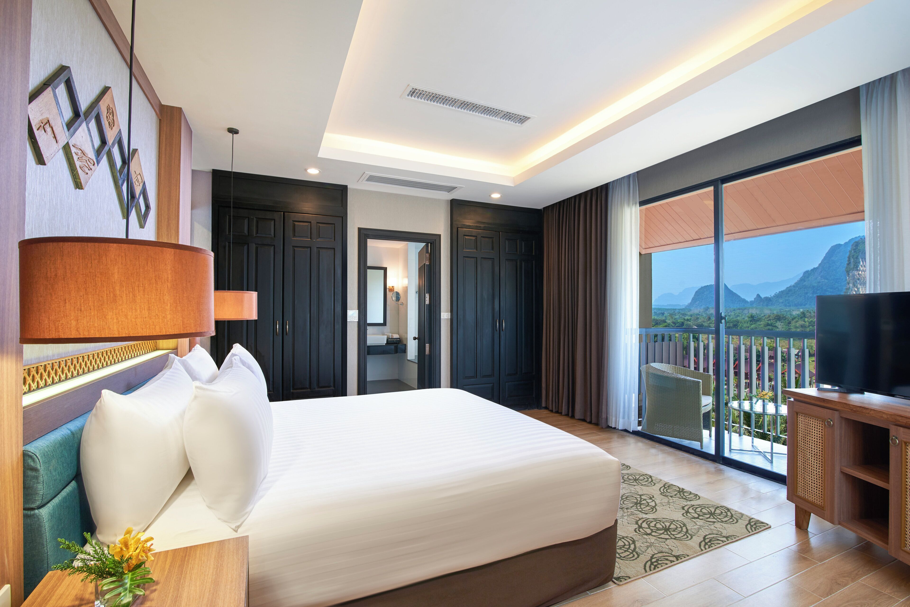 Hotelkamer met een groot bed, een televisie, een balkon met uitzicht en een badkamer zichtbaar door een geopende deur.