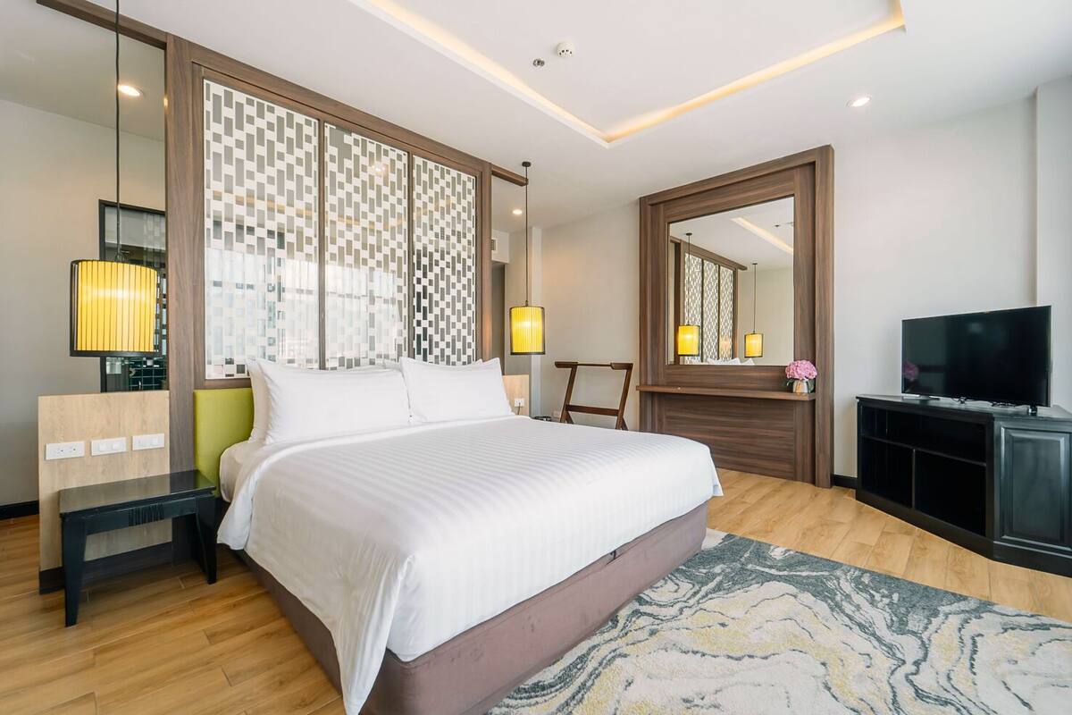 Ein modernes Hotelzimmer mit einem großen Bett, einem Fernseher, einem Schreibtisch und einem Spiegel.