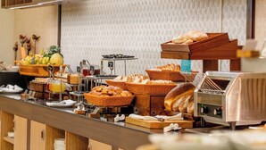 Mostrador de buffet con diversos alimentos, una presentación de frutas y una máquina de café.