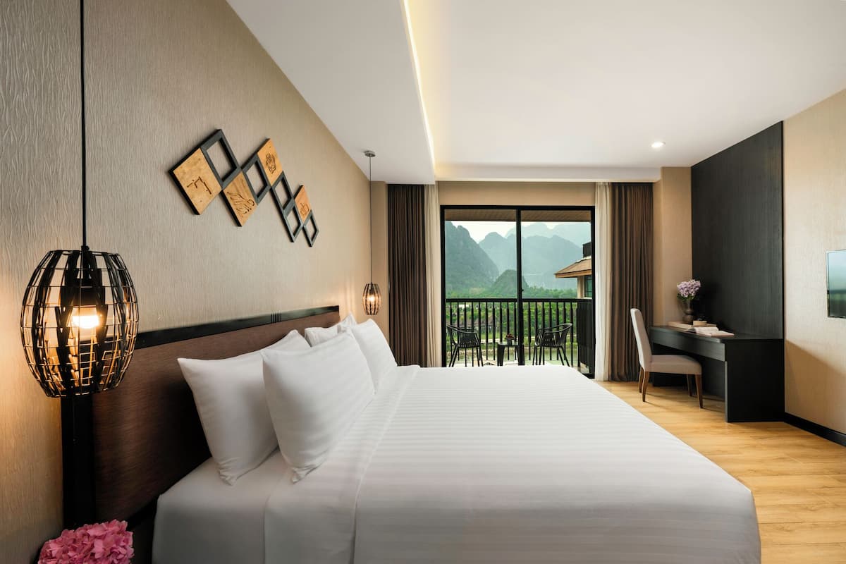 Ein Hotelzimmer mit einem großen Bett, einem Schreibtisch, einem Sessel, einem Fernseher und einem Balkon mit Bergblick.