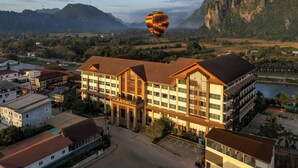 Un hotel con una entrada destacada, un estacionamiento y vistas del paisaje circundante, incluyendo montañas y un río.