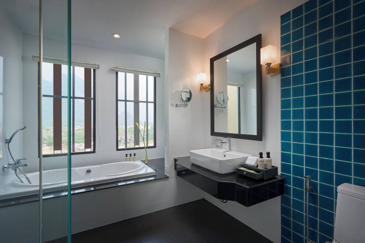 Ein modernes Badezimmer mit Badewanne, zwei Waschbecken, einem großen Spiegel und Blick ins Freie durch große Fenster.