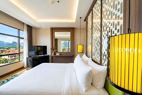 A hotel room with a large bed, a TV, a desk, and a view of the city.