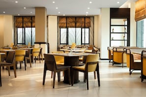 Un restaurant amb diverses taules i cadires, grans finestres amb panells decoratius, i un disseny interior modern.