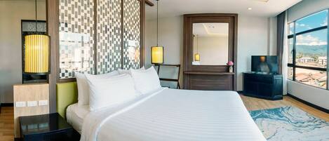 A modern hotel room with a large bed, a desk, a TV, and a view of the city through large windows.