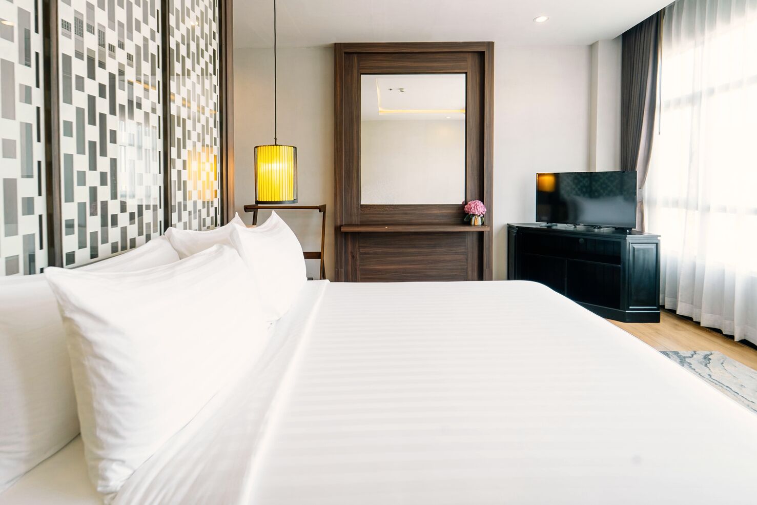 A hotel room with a large bed, a wooden headboard, a television, a mirror, and a decorative lamp.