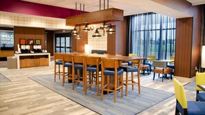 A hotel lobby with a reception desk, a large wooden dining table with chairs, and a view of the outdoors through large windows. - Hampton Inn Lebanon (Lebanon)