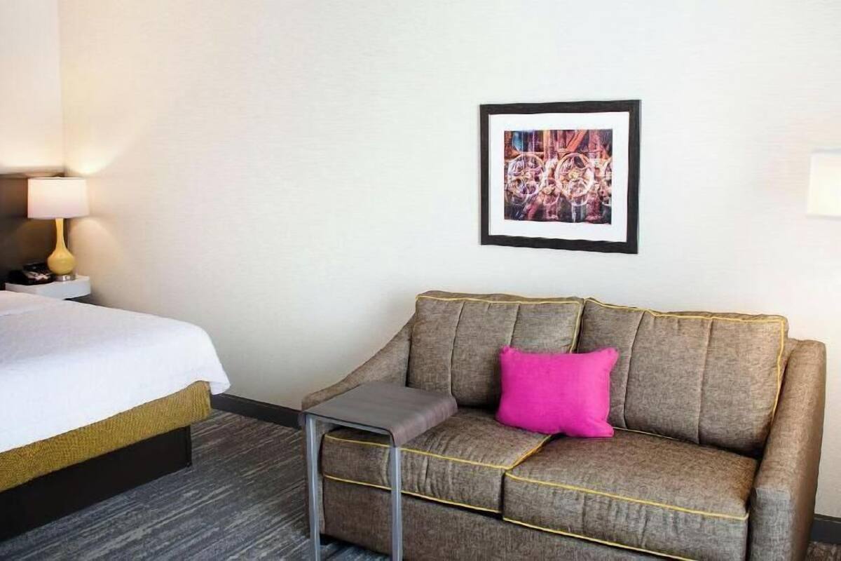 A hotel room with a bed, a sofa, a small table, and a framed picture on the wall.
