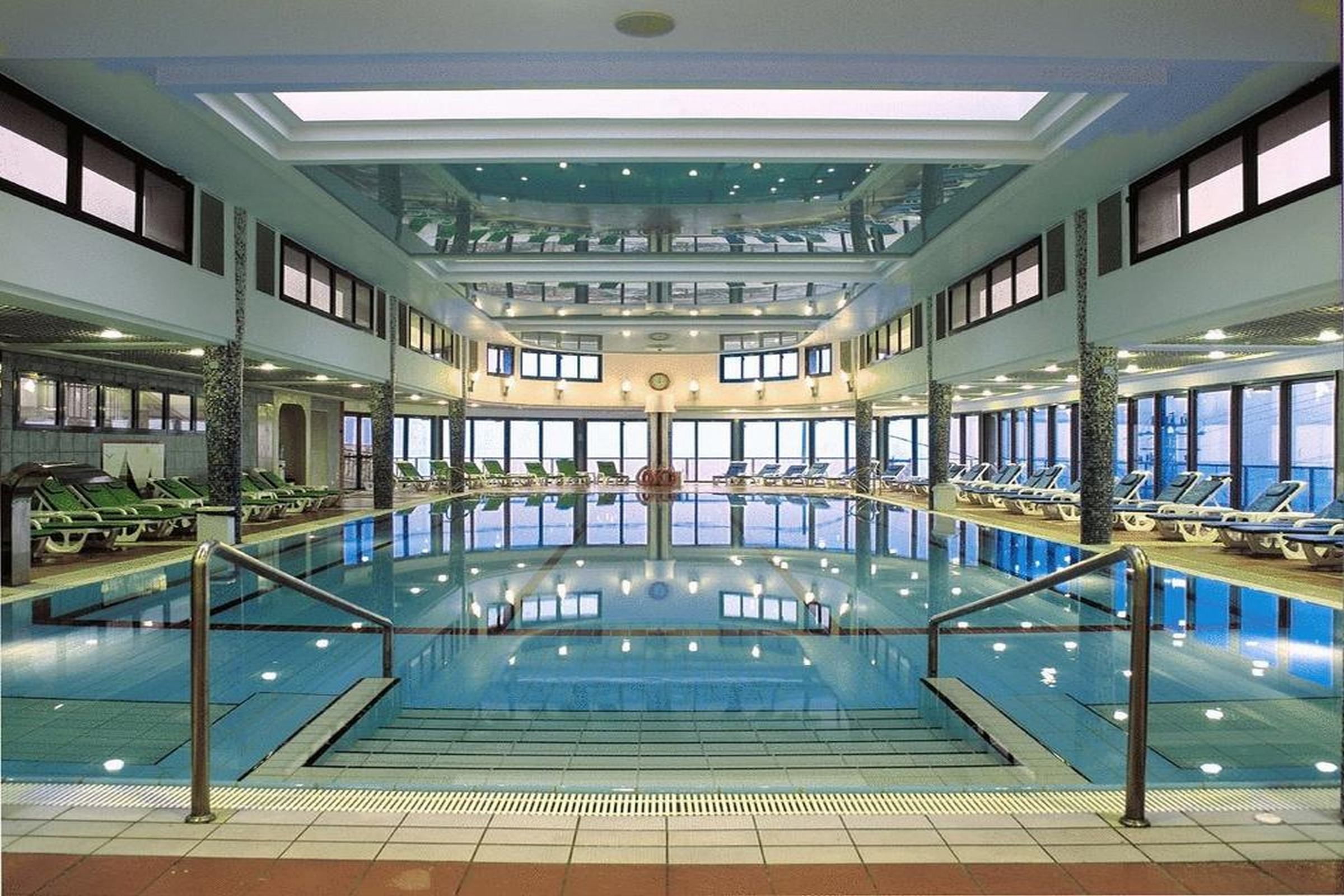 Una amplia piscina interior con varios niveles, ventanas iluminadas por el sol y zonas de descanso.