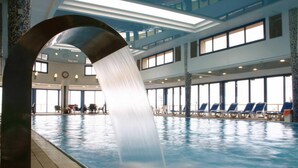 An indoor swimming pool with a water feature, lounge chairs, and a high ceiling with skylights. - Canaan Spa Hotel (Safed)