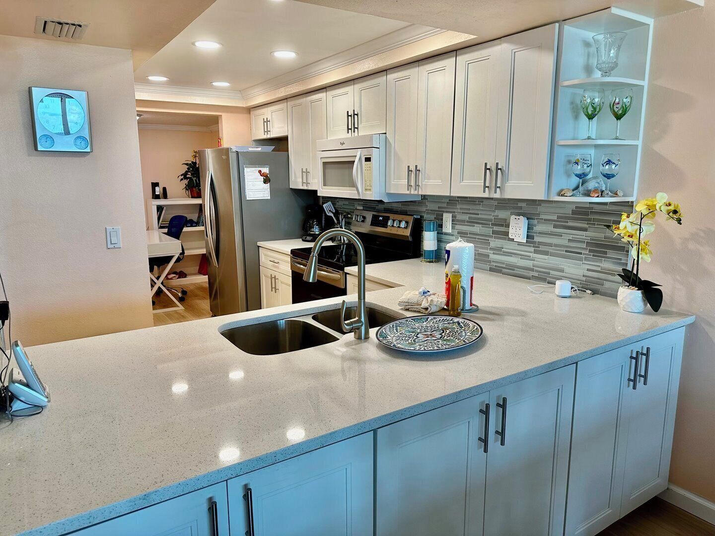 A modern kitchen with white cabinets, a stainless steel refrigerator, a microwave, and a sink.