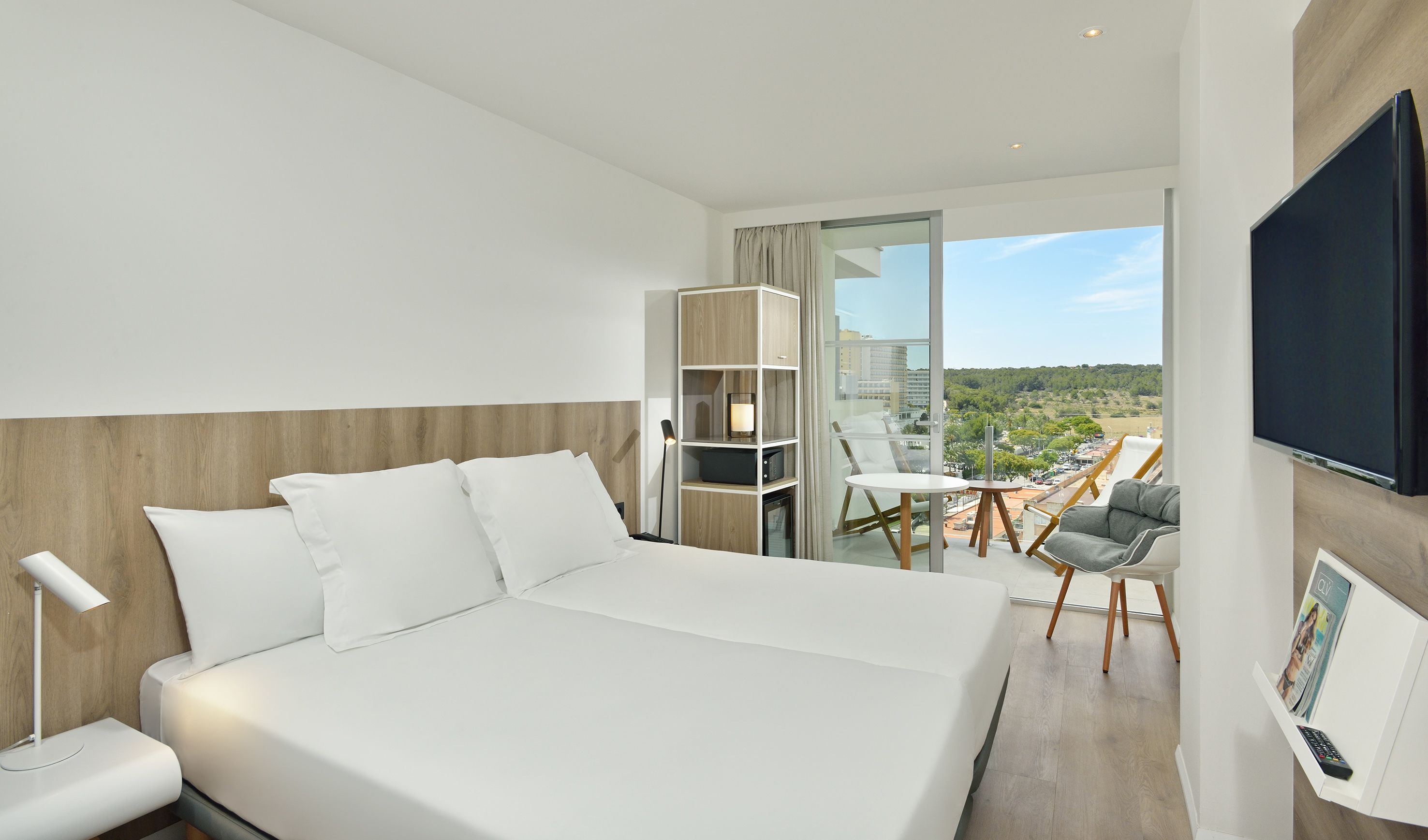 Habitación de hotel moderna con una cama grande, un escritorio con silla, televisión y un balcón con vistas a la ciudad.