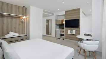 Una habitación de hotel moderna con una cama grande, un armario con espejo, una zona de estar con mesa y sillas, y un televisor montado en la pared.