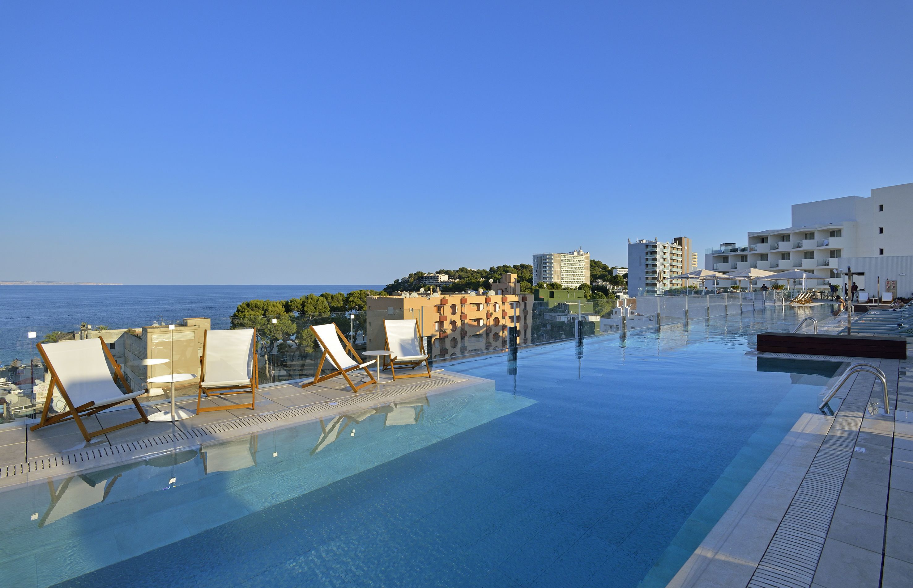 Una piscina a sfioro con lettini, vista libera sul mare e moderni edifici sullo sfondo.