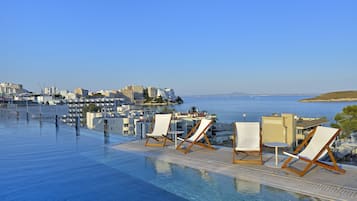 An infinity pool with lounge chairs and a view of the sea and buildings.