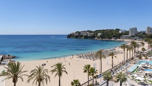 A beach with clear blue water, palm trees, and a pool area with lounge chairs. - INNSiDE by Meliá Calviá Beach (Calvia)