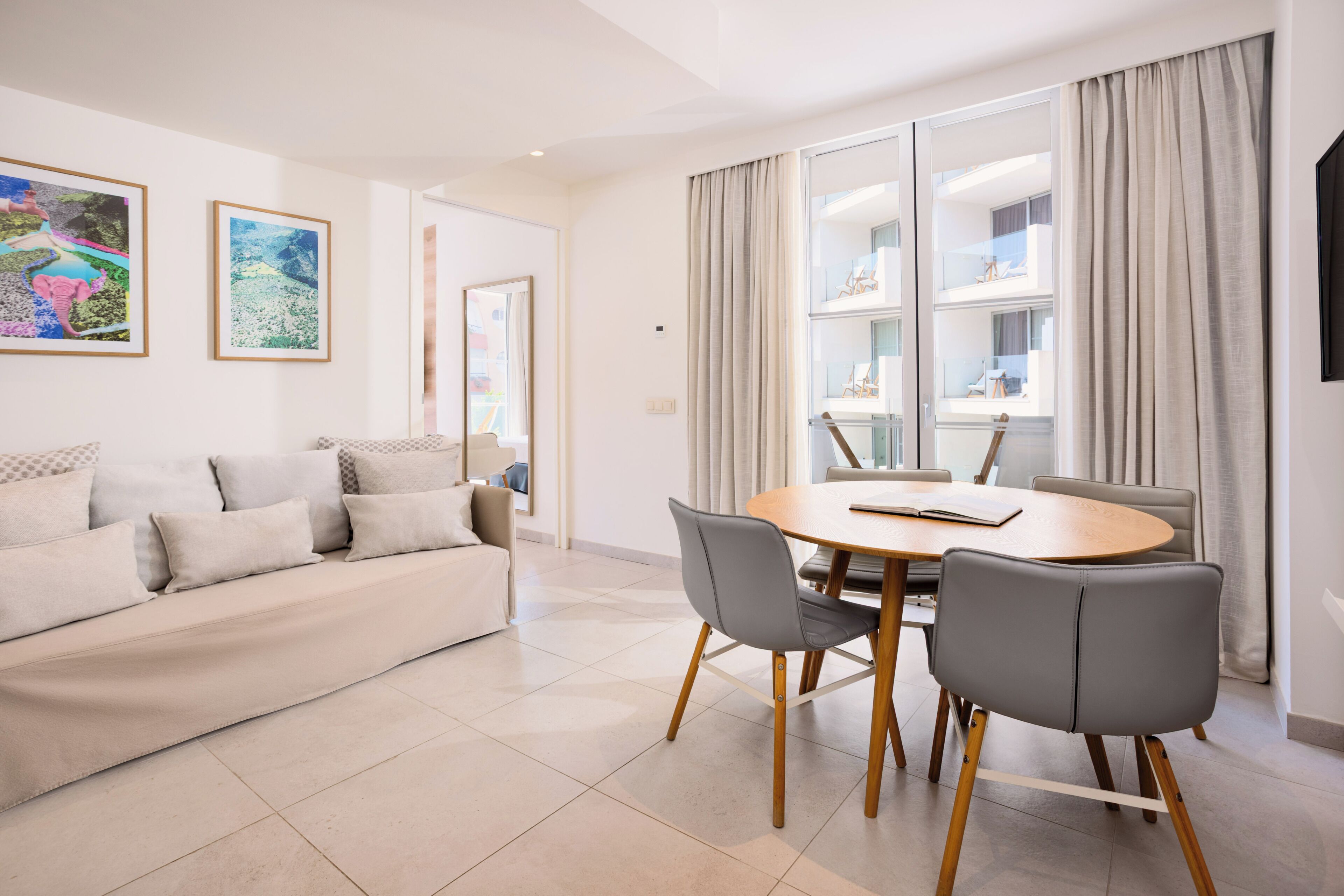 A modern living room with a sofa, a dining table with chairs, and large windows with curtains.