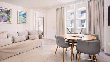 A modern living room with a sofa, a dining table with chairs, and large windows with curtains.