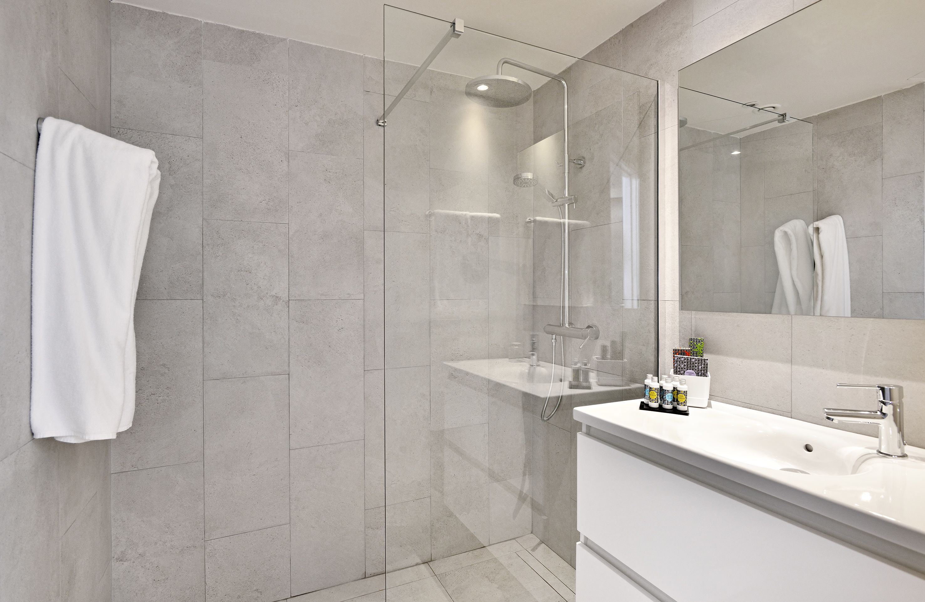 Un baño moderno con ducha de vidrio, lavamanos blanco y espejo grande.