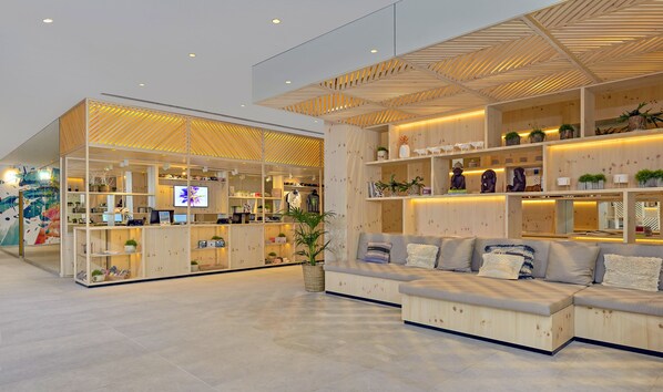 Un interior moderno con mostrador de recepción, zona de estar y estanterías de madera con diversos objetos.
