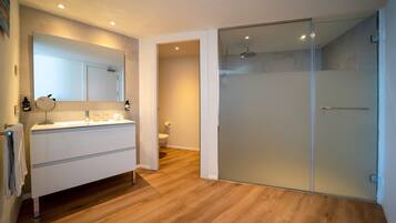 A modern bathroom with a large mirror, a glass shower enclosure, and a wooden floor.