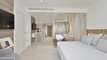 Una habitación de hotel moderna con una cama grande, un televisor montado en la pared, una kitchenette y un baño independiente.