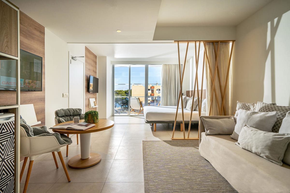 Un salon moderne avec un canapé, une table basse et un téléviseur. Il y a un balcon qui offre une vue sur les immeubles.
