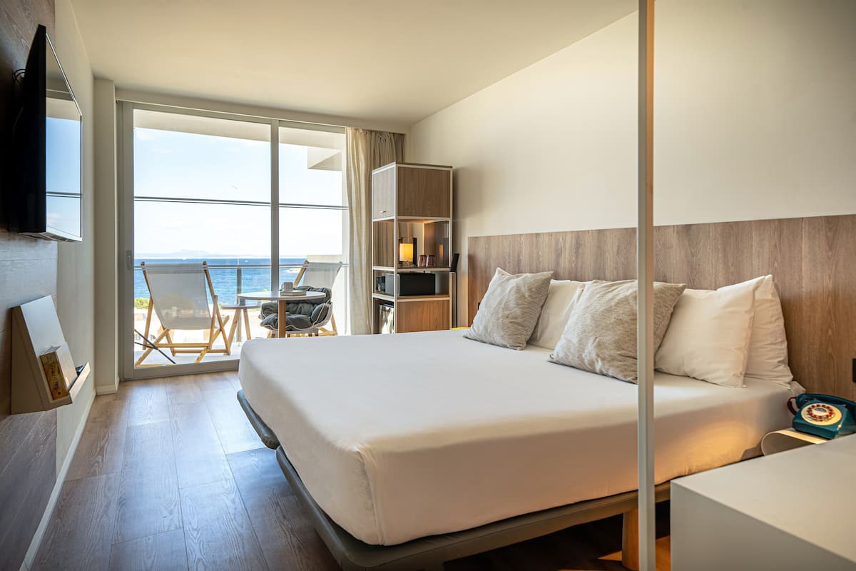 Une chambre d’hôtel avec un grand lit, un téléviseur fixé au mur, une bibliothèque et une vue sur la mer, visible à travers la porte-fenêtre coulissante.