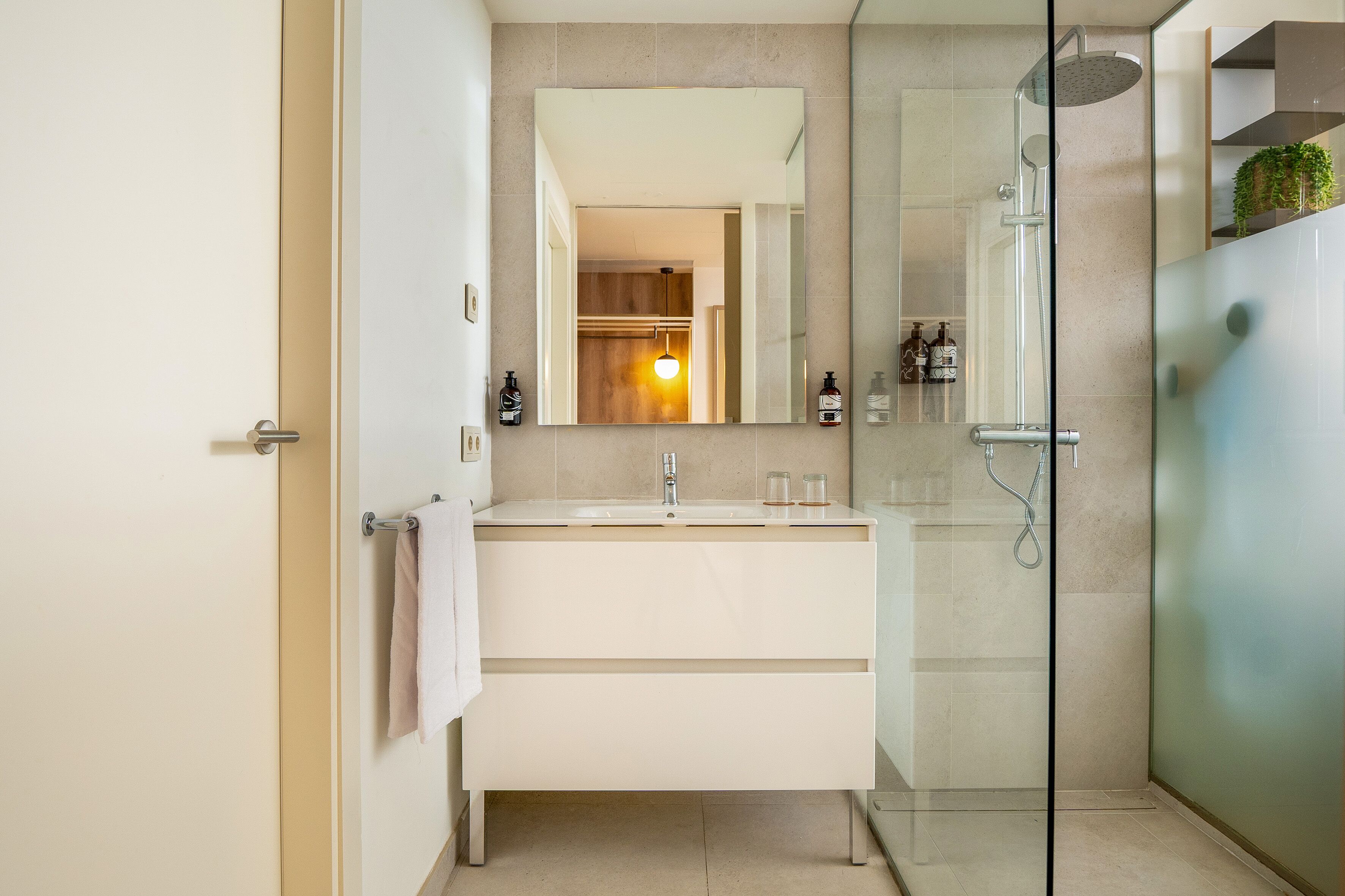 Un baño moderno con cabina de ducha de vidrio, un espejo grande y un tocador blanco.