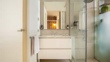 Un baño moderno con cabina de ducha de vidrio, un espejo grande y un tocador blanco.