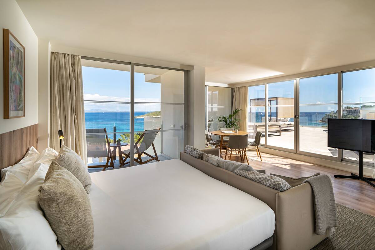 Une chambre d’hôtel moderne dotée d’un grand lit, d’un bureau et d’une télévision. La chambre dispose de grandes fenêtres offrant une vue sur l’océan.