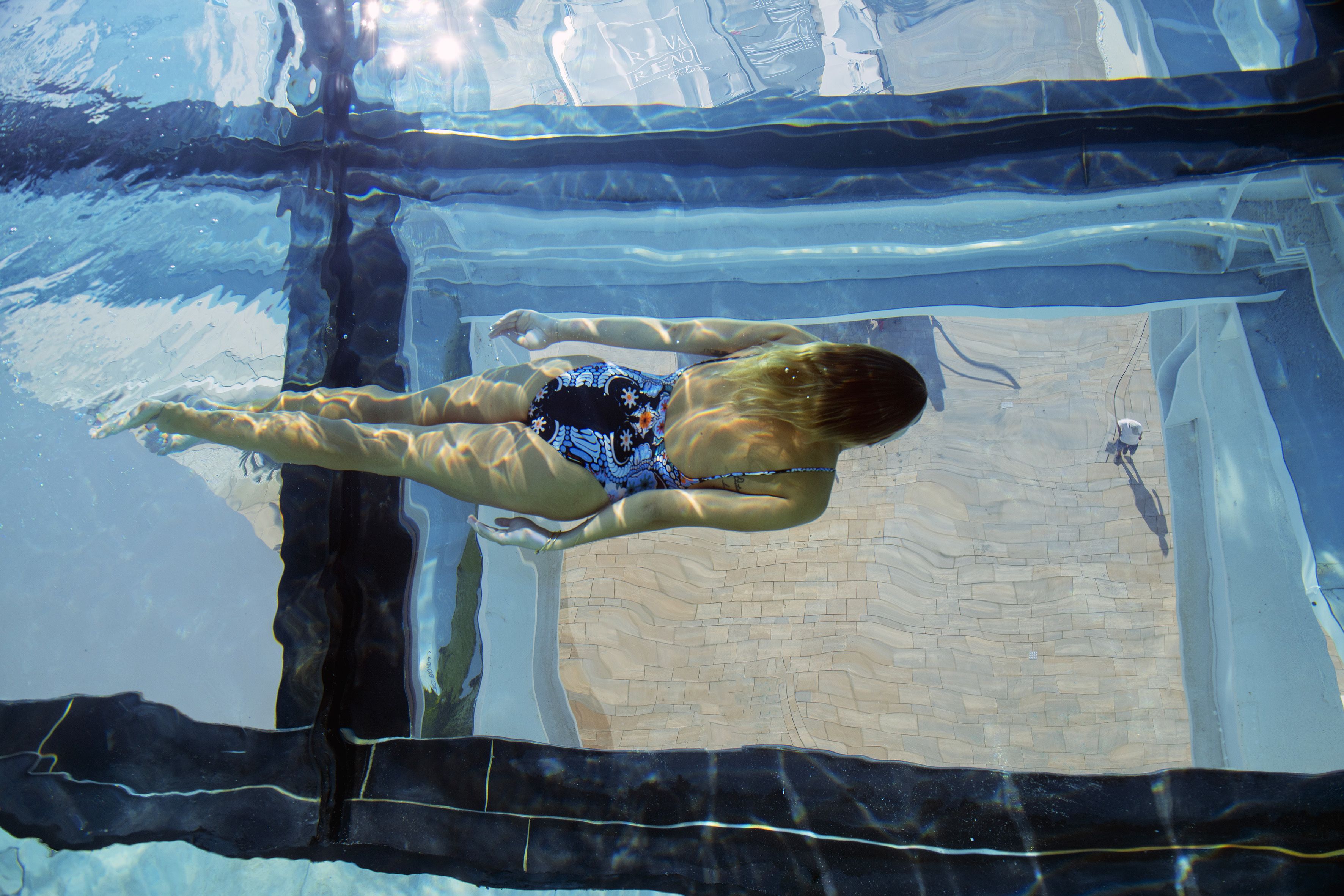 Vista subacuática de una piscina con suelo de baldosas y una persona nadando.