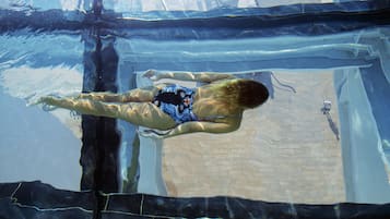 Vista subacuática de una piscina con suelo de baldosas y una persona nadando.