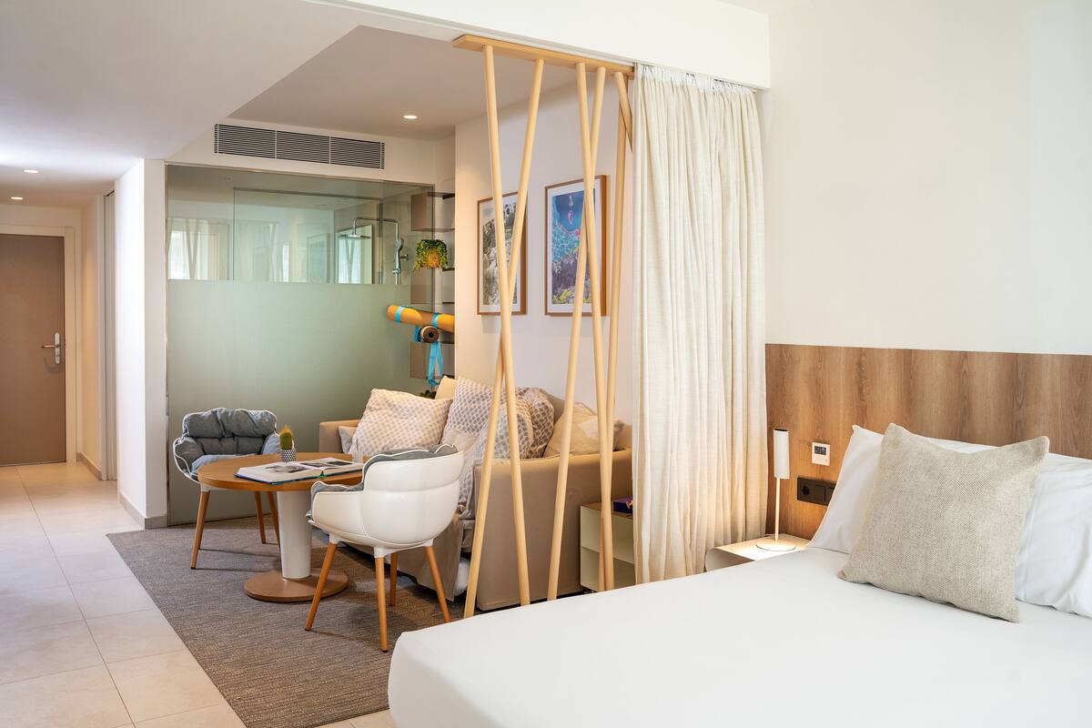 Une chambre d’hôtel moderne avec un lit, un canapé, une petite table et une chaise. Un rideau sépare le lit du canapé.