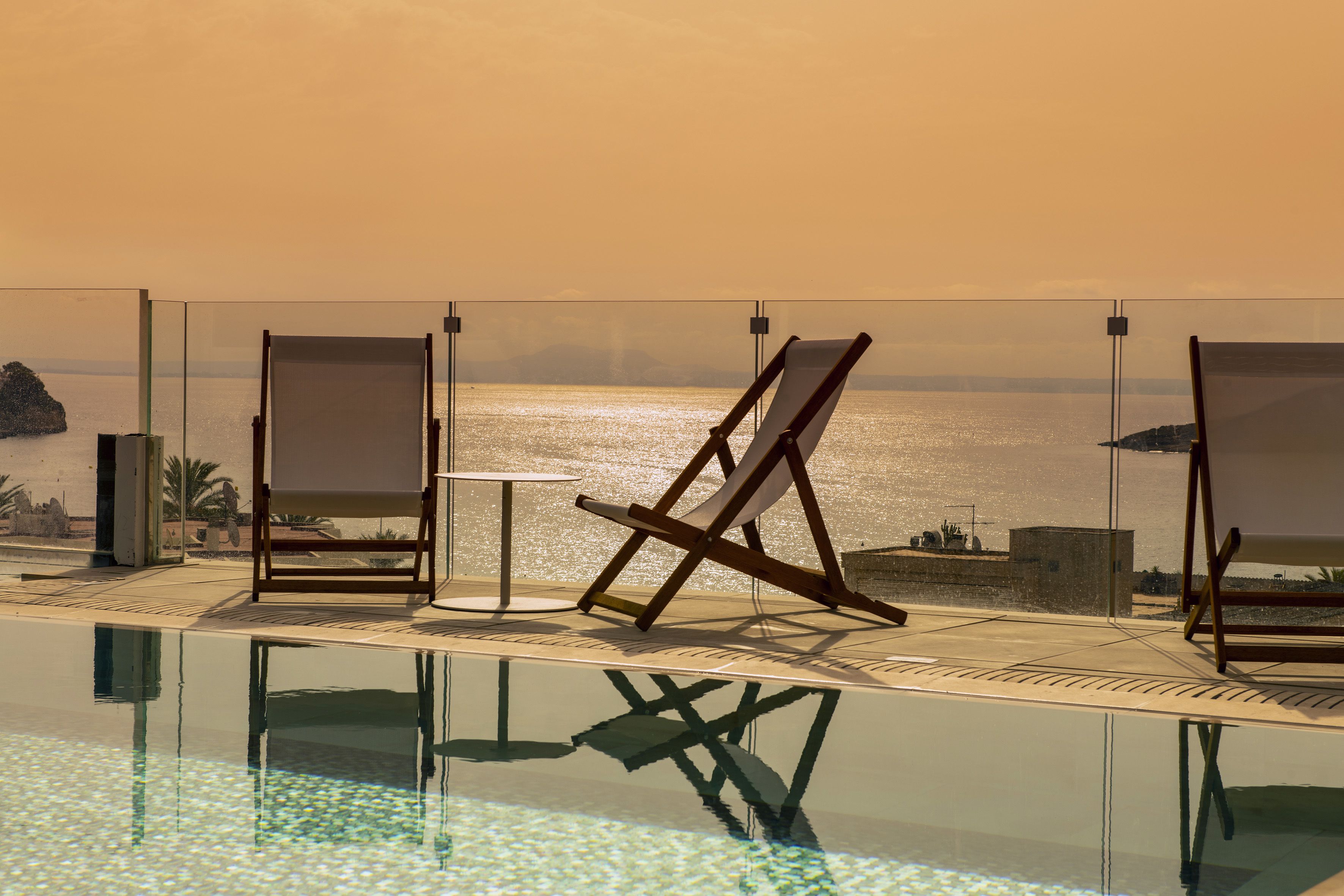 A poolside area with lounge chairs and a table, overlooking a body of water and distant land.