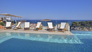 A poolside area with lounge chairs and umbrellas, overlooking a clear blue sea and a distant island. - INNSiDE by Meliá Calviá Beach (Calvia)