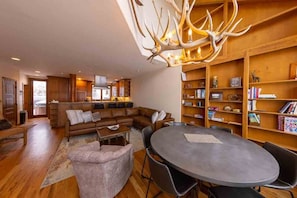 A modern living room with a sectional sofa, a round dining table, and a wooden bookshelf.